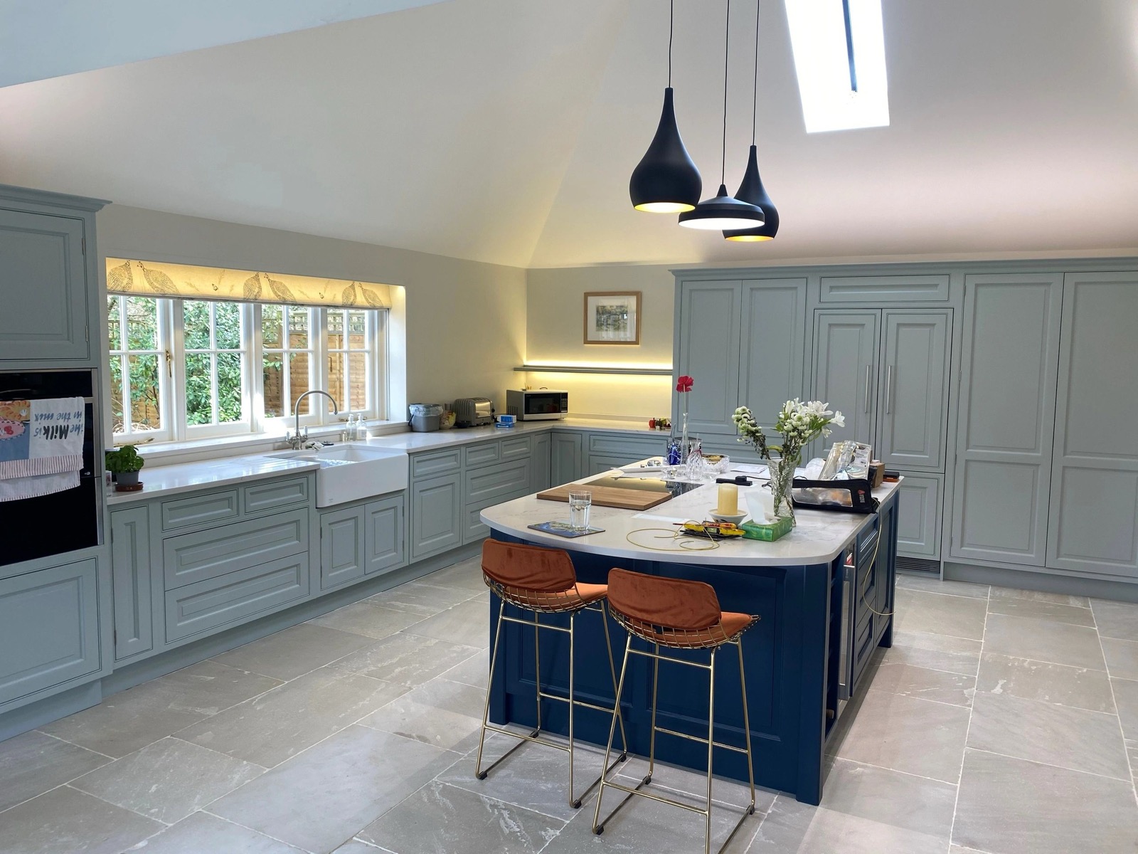A kitchen with pendant lights over a navy island and light under the wall cabinets