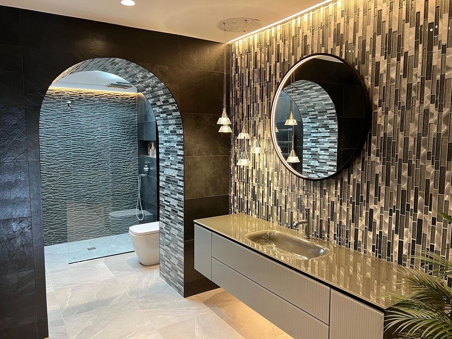 A tiled bathroom with lighting along the top of the wall and an arched shower opening