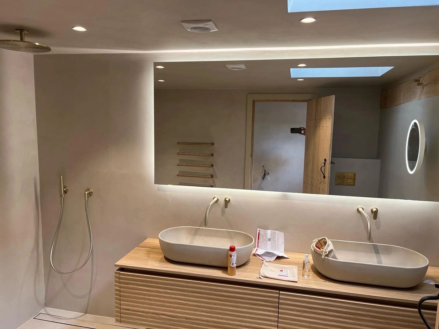 A bathroom with a backlit mirror over twin basins and recessed ceiling lights